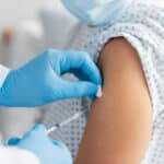 Ein Arzt verabreicht einem Patienten eine Injektion in den Oberarm, während der Patient einen Krankenhauskittel trägt.
