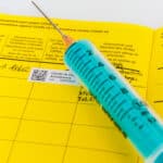 Eine blaue Spritze liegt auf einem gelben Impfausweis, in dem ein Covid-19-Impftermin vermerkt ist.