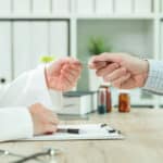 Nahaufnahme der Hand eines Arztes, welche einem Patienten die Krankenkassenkarte zurück gibt