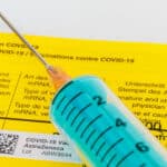 Nahaufnahme einer blauen Spritze mit einem gelben Impfausweis